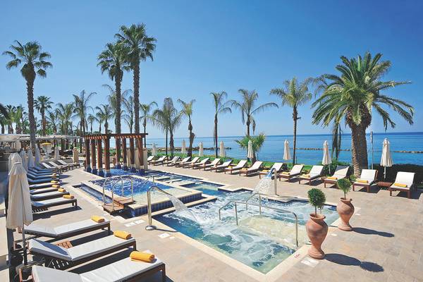 Außenpoolbereich des Alexander The Great Hotels mit Loungeliegen, Palmen und Meerblick.