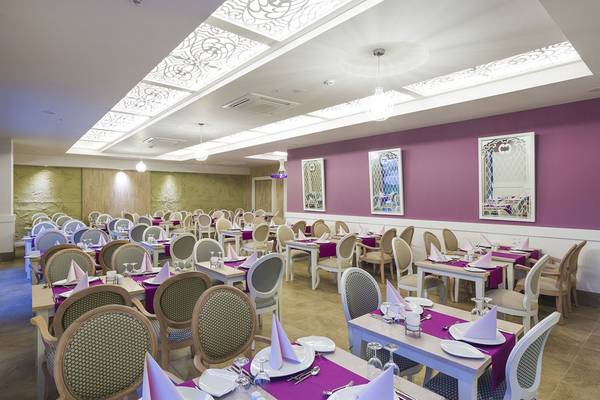 Innenraum des Restaurants im Terrace Elite Resort mit violetten Wänden und geometrischen Deckenleuchten.