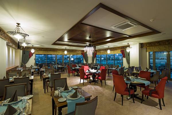 Innenbereich des Restaurants im Terrace Elite Resort mit vielen Tischen und Stühlen, Fenstern und Kronleuchtern.