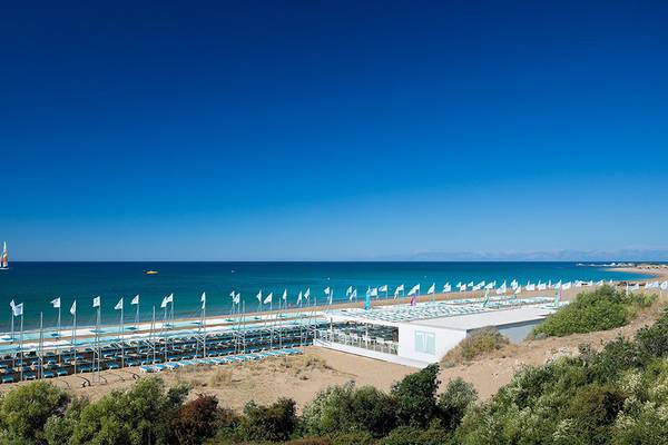 Terrasse Elite Resort Strand mit vielen Sonnenliegen, Flaggen und einer weißen Struktur.