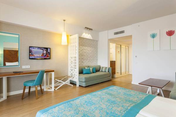 Innenansicht eines Zimmers im Terrace Elite Resort mit Bett, Schreibtisch, Fernseher und Sofa.