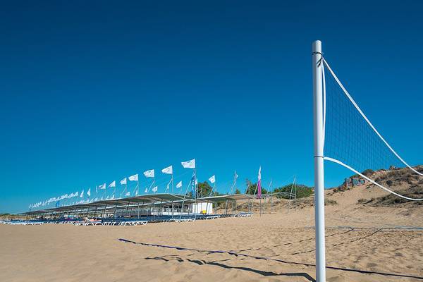 Ein Volleyballnetz auf dem Strand des Terrace Elite Resorts mit vielen Sonnenliegen und Fahnen im Hintergrund.
