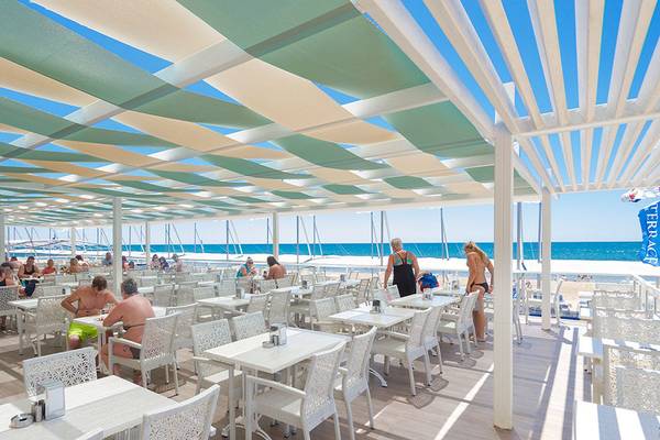 Terrasse des Elite Resorts mit einem Blick auf das Strandrestaurant und Gäste, die drinnen und draußen sitzen.