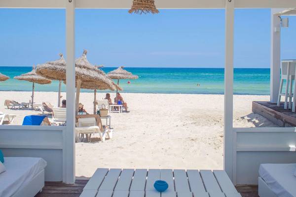Blick auf den Strand des Radisson Blu Palace Resort in Djerba mit Gästen unter Sonnenschirmen.