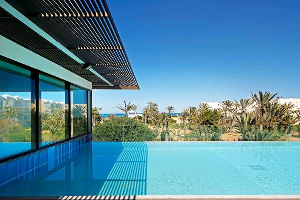 Außenpool des Radisson Blu Palace Resort & Thalasso, Djerba mit Palmen und Meer im Hintergrund