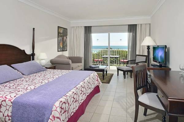 Hotelzimmer mit Meerblick und Balkon, Bett, Stühle, Schreibtisch und Fernseher.