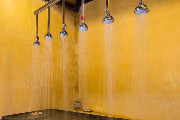 Ein Raum mit mehreren Duschköpfen, die Wasser sprühen, an einer gelben Wand.