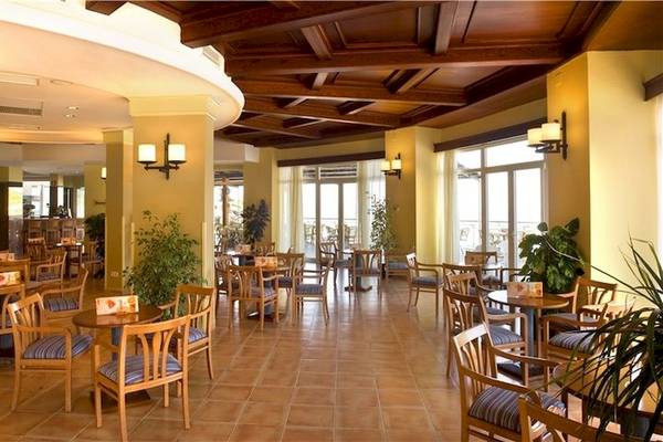 Innenbereich des Universal Hotel Aquamarin Restaurants mit runden Tischen und Stühlen, bepflanzten Ecken und Holzdecken.