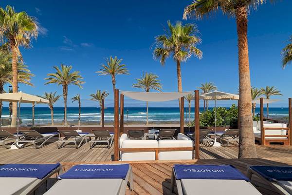 Außenterrasse des H10 Conquistador Hotels mit Lounge-Liegestühlen, Sonnenschirmen und Meerblick.