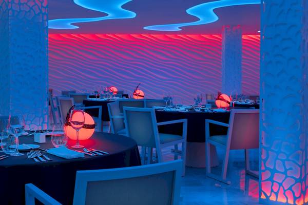 Innenraum des H10 Conquistador Hotels mit blauen und roten Lichtern und gedeckten Tischen.
