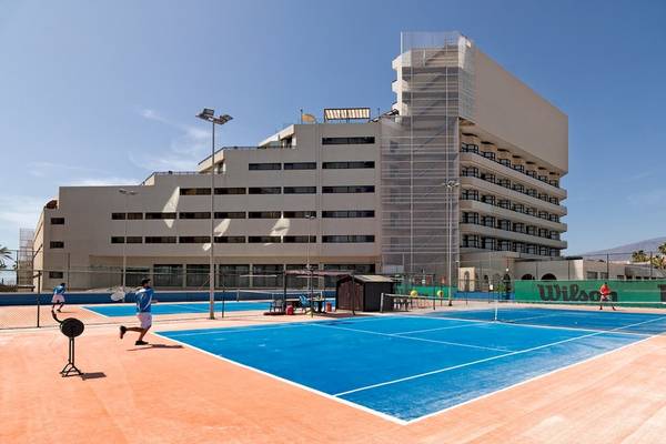 Tennisplatz vor dem H10 Conquistador Hotel mit Spielern und Gebäude im Hintergrund.