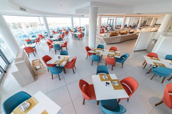 Innenansicht des Restaurants im Ramla Bay Resort mit vielen blauen und orangefarbenen Stühlen und Tischen.