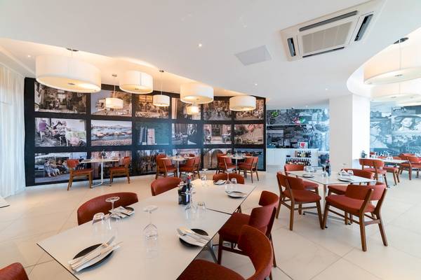 Innenansicht des Restaurants im Ramla Bay Resort mit mehreren Tischen und Stühlen, Fotowänden und Deckenlampen.