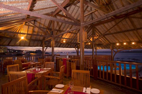 Innenansicht des Restaurants im Ramla Bay Resort mit Holzmöbeln und Blick auf den Pool.
