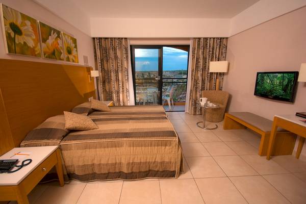 Innenansicht eines Hotelzimmers im Ramla Bay Resort mit zwei Betten, Fernseher und Balkon.
