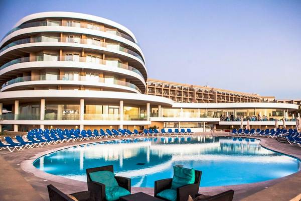 Poolbereich des Ramla Bay Resorts mit runden Gebäuden und blauen Sonnenliegen.