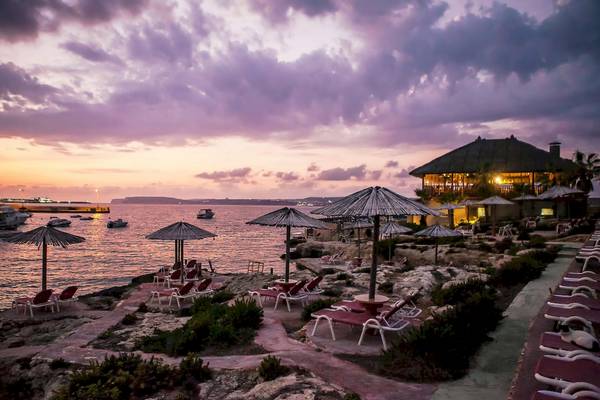 Abendstimmung am Ramla Bay Resort mit Sonnenuntergang, Strandliegen und Booten im Wasser.