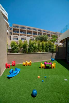 Kinderspielplatz im Ramla Bay Resort mit Spielzeug und Gebäude im Hintergrund.