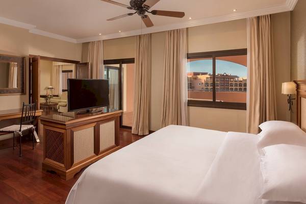 Innenansicht eines Hotelzimmers im Sheraton Fuerteventura Beach, Golf & Spa Resort mit Fernseher, Fenster und Bett.