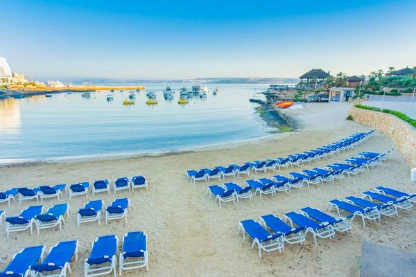 Strand mit vielen blauen Liegestühlen und Booten im Hintergrund, Ramla Bay Resort