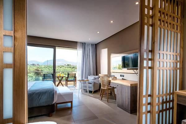 Innenansicht eines Hotelzimmers im Stella Palace Resort & Spa mit Bett, Schreibtisch, Fernseher und Terrassenblick.