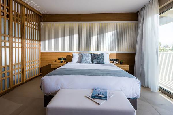 Ein elegantes Schlafzimmer im Stella Palace Resort & Spa mit Bett, Kissen und Zeitschriften auf einem weißen Ottoman.