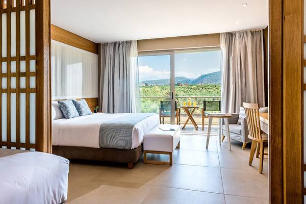 Innenansicht eines Zimmers im Stella Palace Resort & Spa mit zwei Betten, Tisch, Stühlen und einem Balkon.