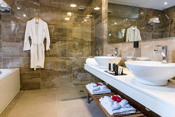 Ein elegantes Badezimmer im Stella Palace Resort & Spa mit Marmorwänden, zwei Waschbecken und einer Badewanne.