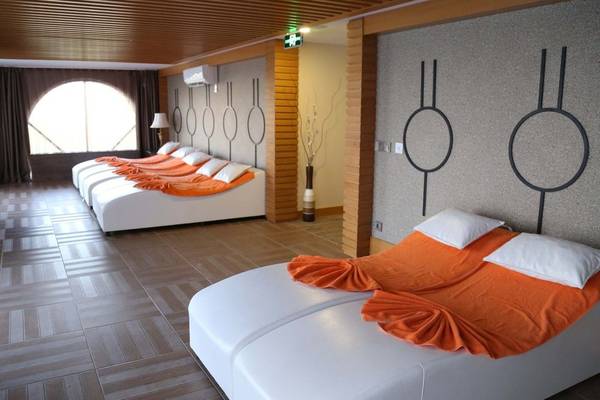 Ein modernes Schlafzimmer im J'adore Deluxe Hotel & Spa mit mehreren weißen Betten und orangefarbenen Decken.