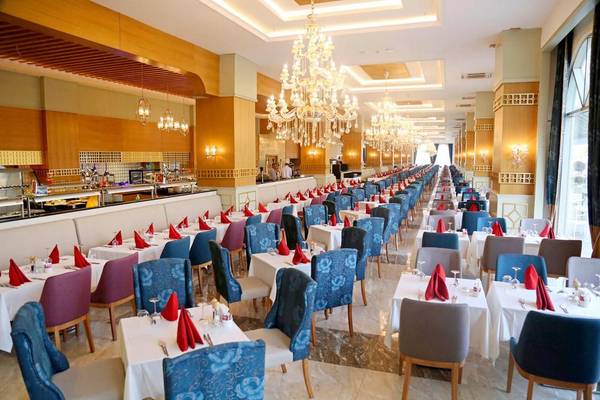 Innenansicht des Restaurants im J'adore Deluxe Hotel & Spa mit gedeckten Tischen, Kronleuchtern und einer Bar im Hintergrund.