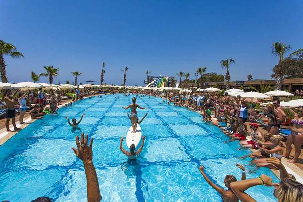 Pool-Party im Eftalia Holiday Village mit vielen Gästen und einer Person auf einem Surfbrett.