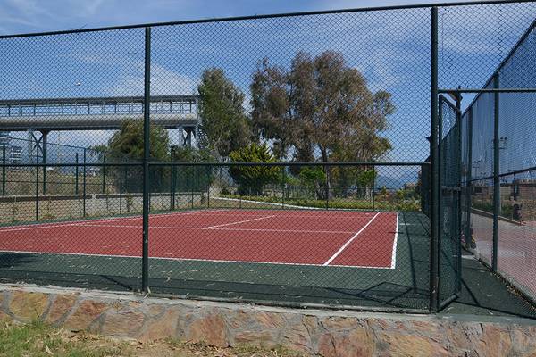 Tennisplatz mit Zaun und Ausblick auf eine Brücke und Bäume
