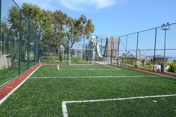 Tennisplatz im Eftalia Holiday Village mit grünem Kunstrasen und umlaufender Umzäunung.