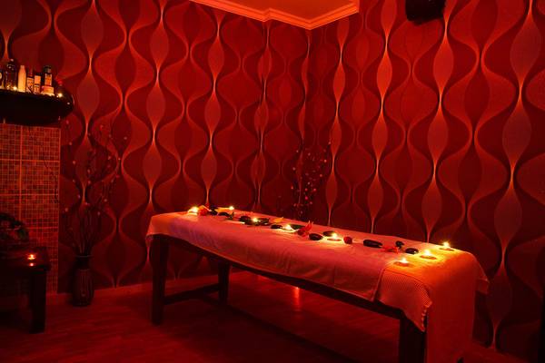 Ein roter Raum mit einem Massagetisch, Kerzen und einem roten Wanddesign.