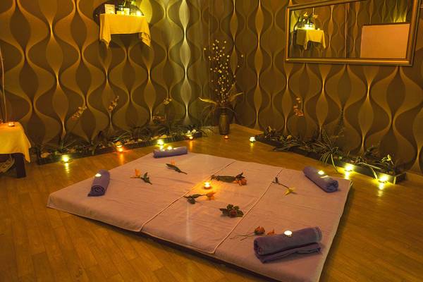 Massagebereich im Eftalia Holiday Village mit Kerzen, Blumen und gerollten Handtüchern auf einem violetten Tisch.
