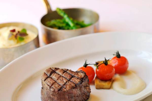 Ein Steak auf einem weißen Teller im Park Hyatt Abu Dhabi Hotel & Villas, neben Tomaten und Beilagen.