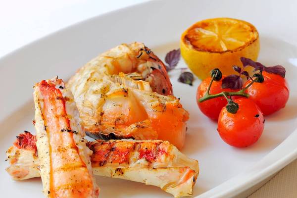 Gegrillte Garnelen und Krebse auf einem weißen Teller mit Zitrone und Tomaten