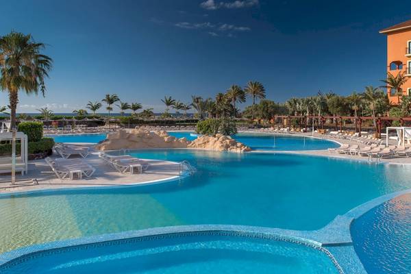Außenpool im Sheraton Fuerteventura Beach, Golf & Spa Resort mit Lounge-Liegen und Palmen.