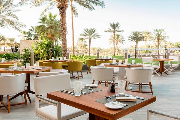 Außenterrasse des Le Royal Meridien Beach Resort & Spa mit Tischen und Stühlen unter Palmen