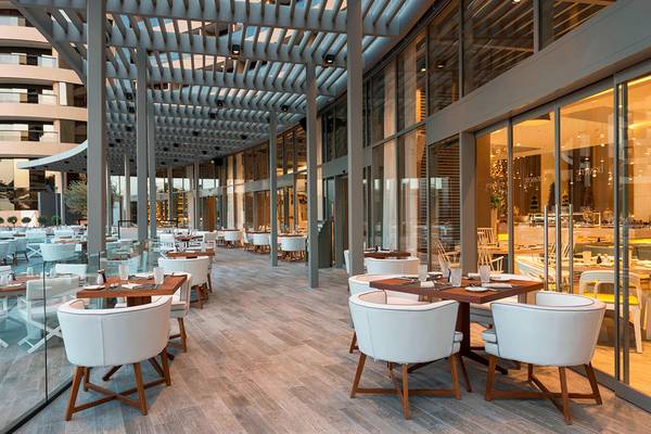 Innenbereich des Restaurants im Le Royal Meridien Beach Resort & Spa mit weißen Möbeln und Holzboden.