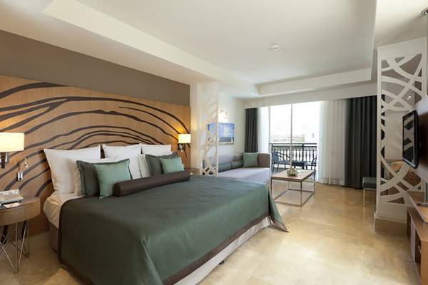 Innenansicht eines eleganten Hotelzimmers im Paloma Oceana Hotel mit Bett, Wohnzimmerbereich und Terrasse.