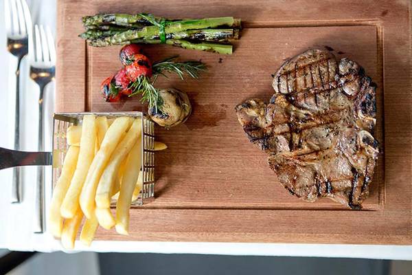 Ein Steak-Teller mit Pommes, Spargel, Tomaten und Rosmarin auf einem Holzbrett.