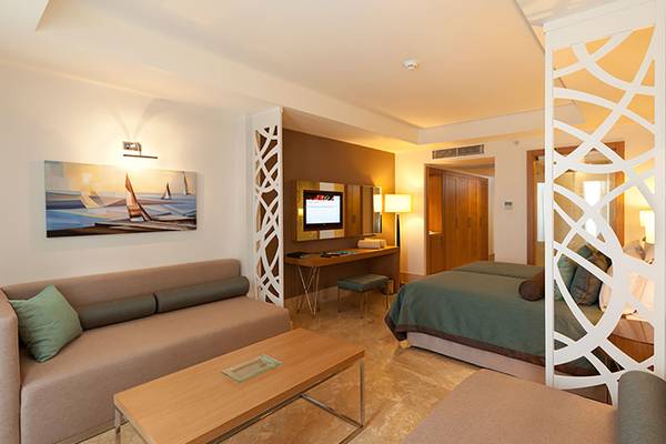 Innenansicht einer Suite im Paloma Oceana Hotel mit Wohnzimmer und Schlafzimmerbereich.
