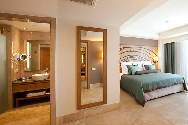 Innenansicht eines Schlafzimmers im Paloma Oceana Hotel mit Bett, Spiegel und Waschtisch.