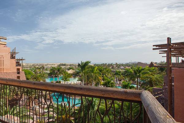 Blick von einem Hotelbalkon auf den Pool und die Landschaft mit Gebäuden und Palmen.
