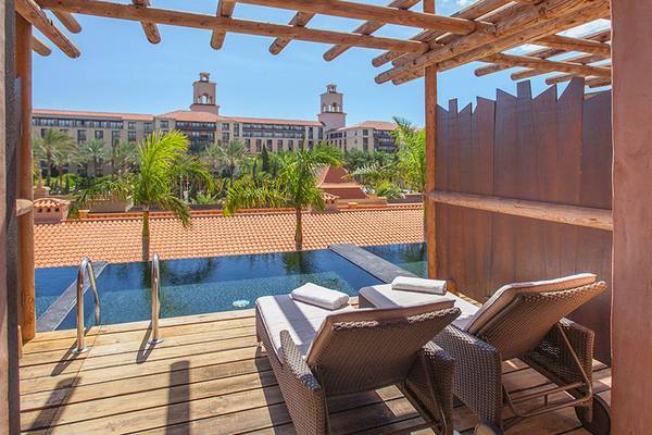 Aussicht auf den Pool-Lounge-Bereich des Lopesan Baobab Resort mit Lounge-Stuhl und Sonnenschirm.