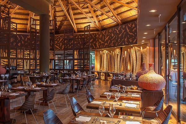Innenansicht des Lopesan Baobab Resort Restaurants mit Holztischen, Stühlen und dekorativen Vasen.