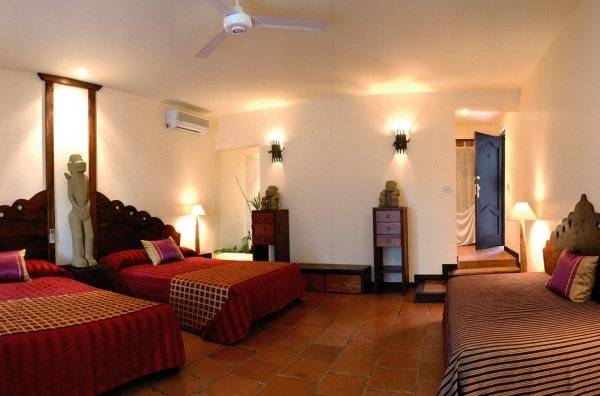 Schlafzimmer im Jardin del Eden Boutique Hotel mit drei Betten, Holzbettrahmen und dekorativen Elementen.