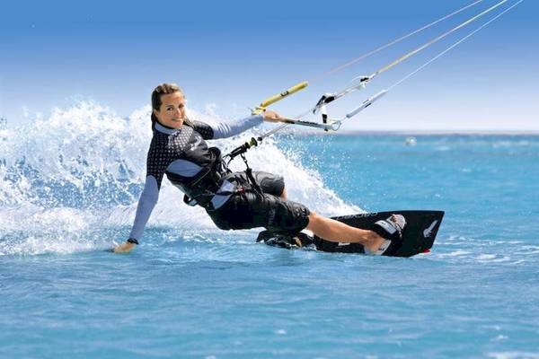 Frau kitesurfen im Ozean mit blauem Himmel und Wellen im Hintergrund.