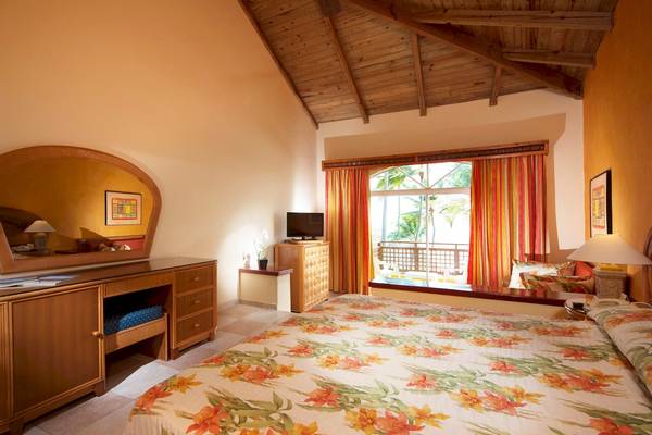 Innenansicht eines Schlafzimmers im Caribe Deluxe Princess Hotel mit blumigen Bettlaken und Blick auf das Meer.